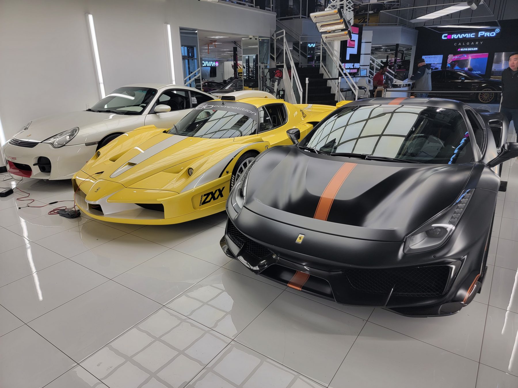 Three Ferraris in a private showroom — a 488 Pista, a yellow FXX-K, and a white Porsche GT2 RS
