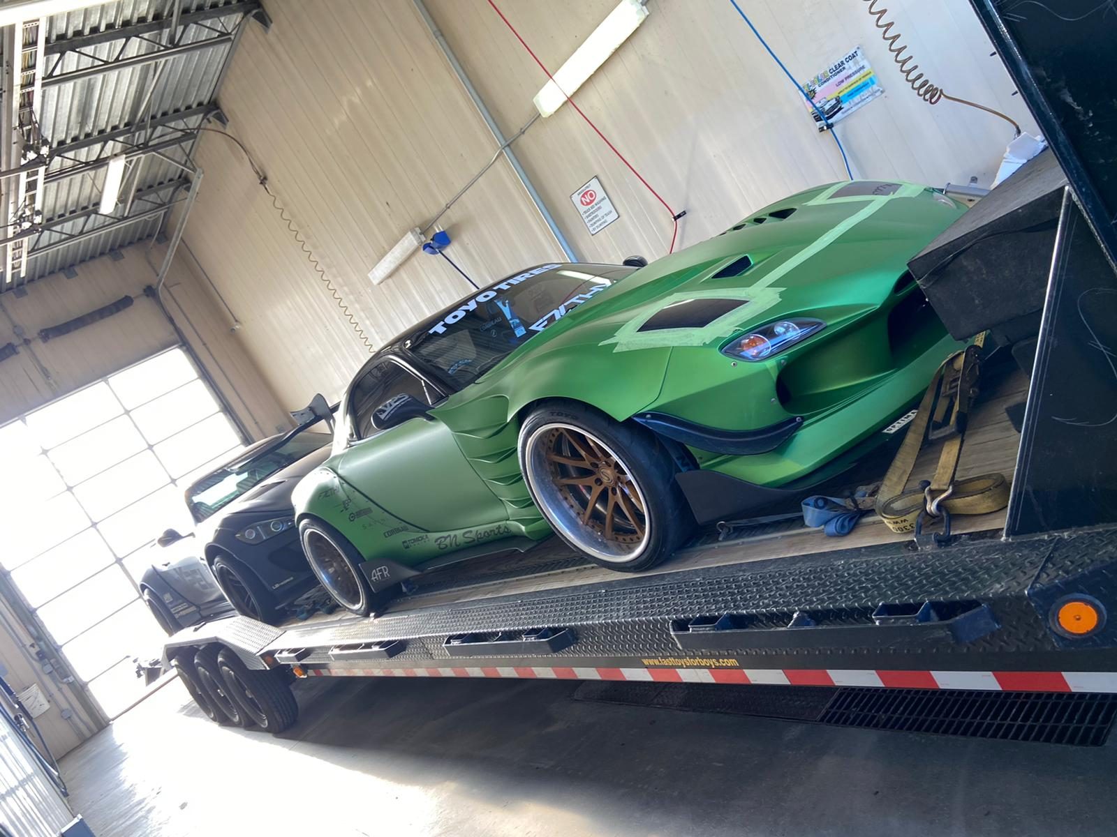 A wide-body Toyota Supra in metallic green with bronze wheels, on a transport trailer