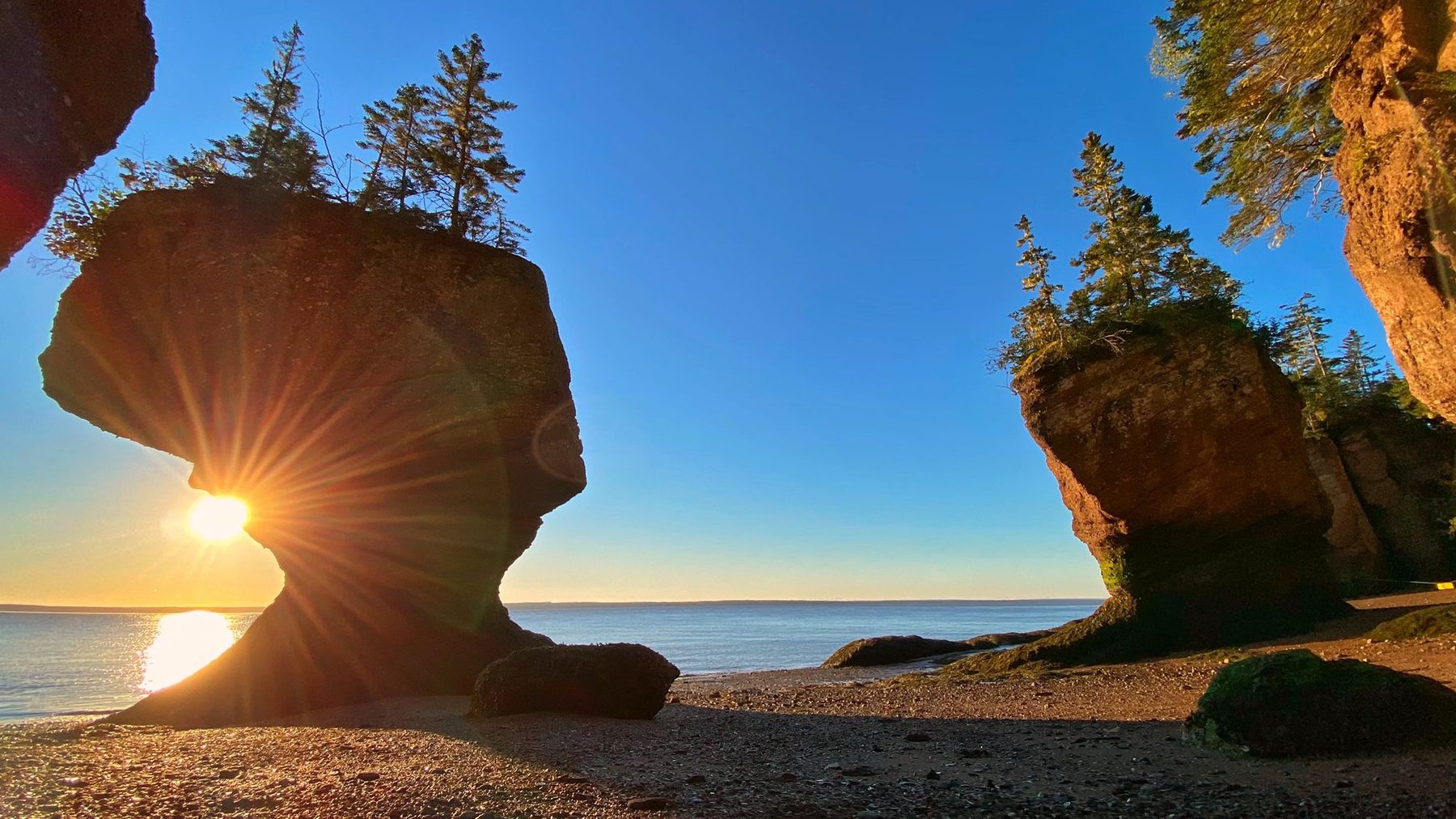 The Hopewell Rocks at sunrise on the Bay of Fundy, sun rays flaring through a sea-stack