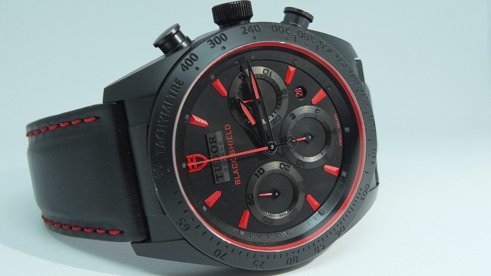 Tudor Black Shield chronograph with red accents on a leather strap, three-quarter view