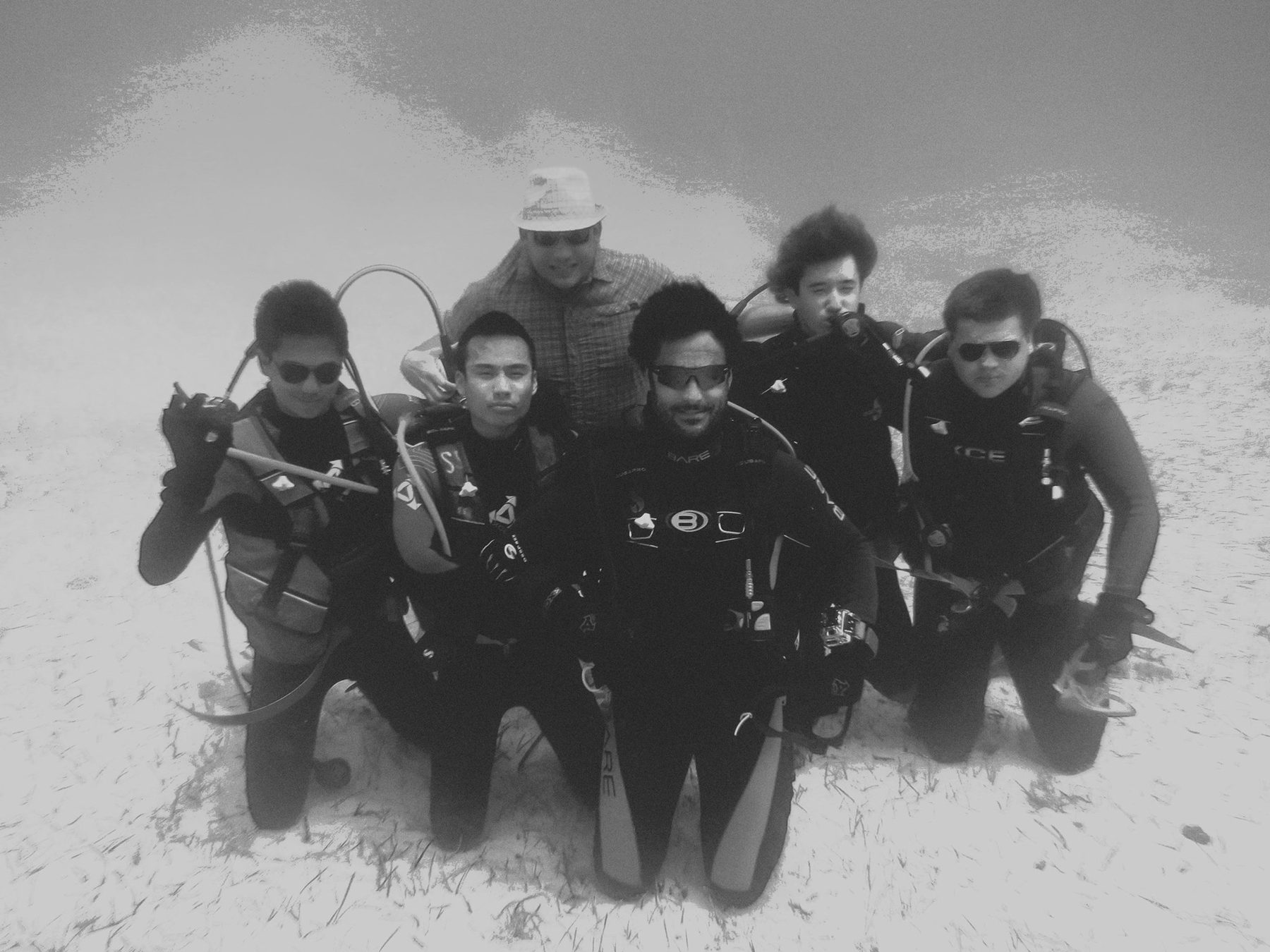 Black and white photograph of a dive team kneeling on the sand below