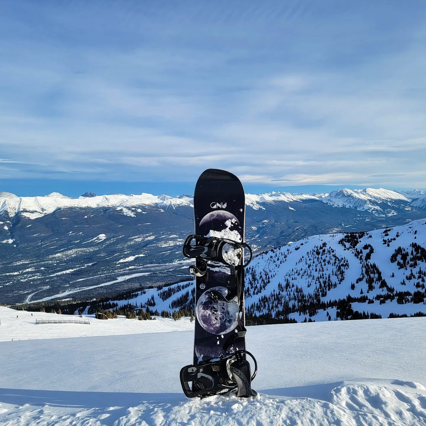 A snowboard standing alone in the snow at a high alpine ridge