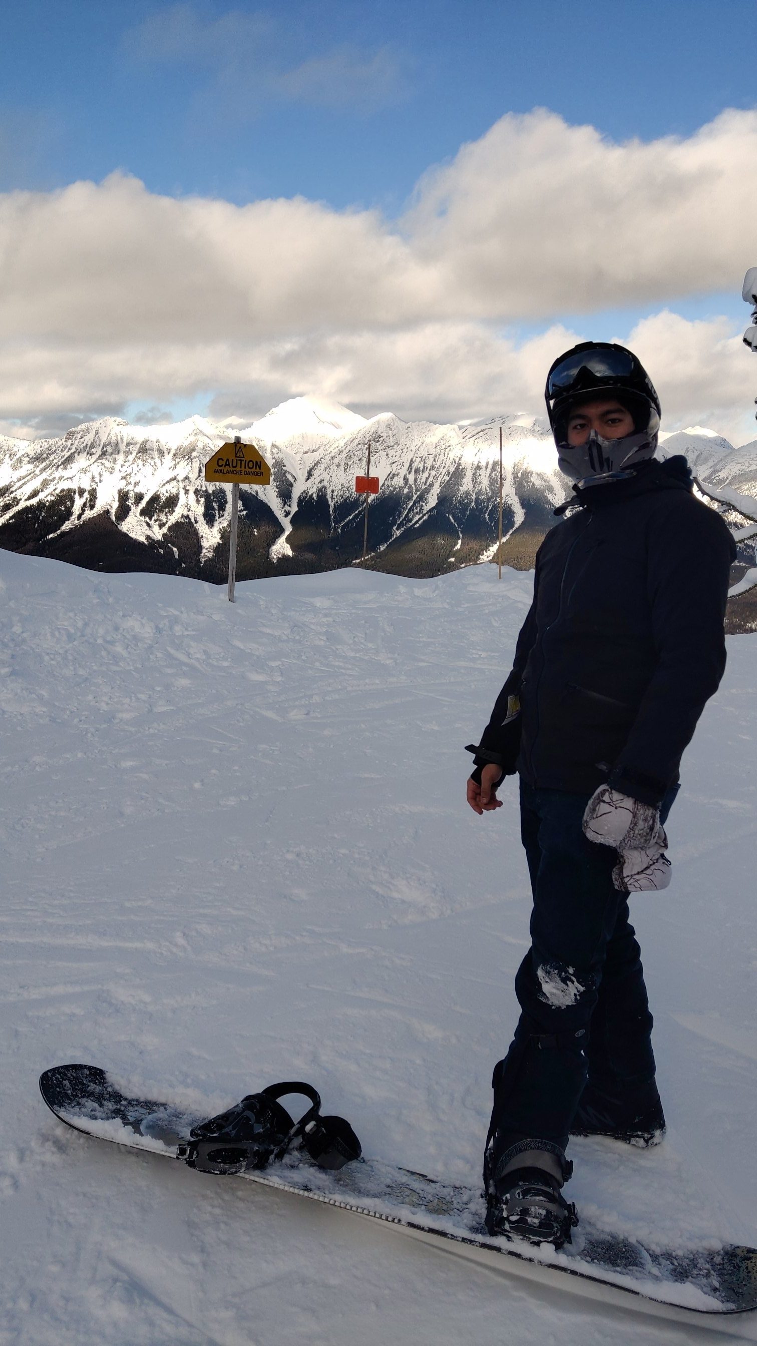 A snowboarder at a mountain summit with the Rockies behind