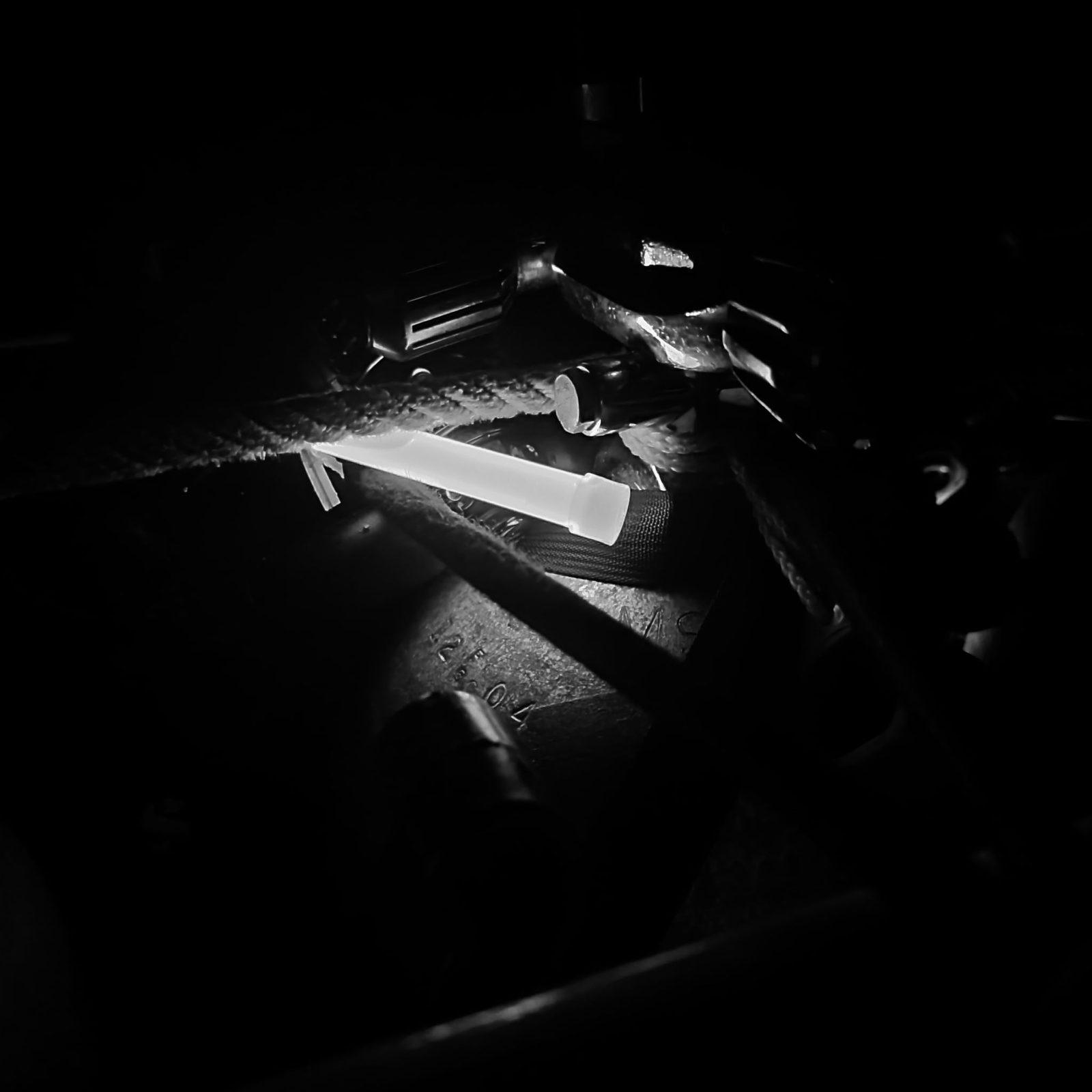 A black and white close-up of a glowstick lighting up rope and rigging